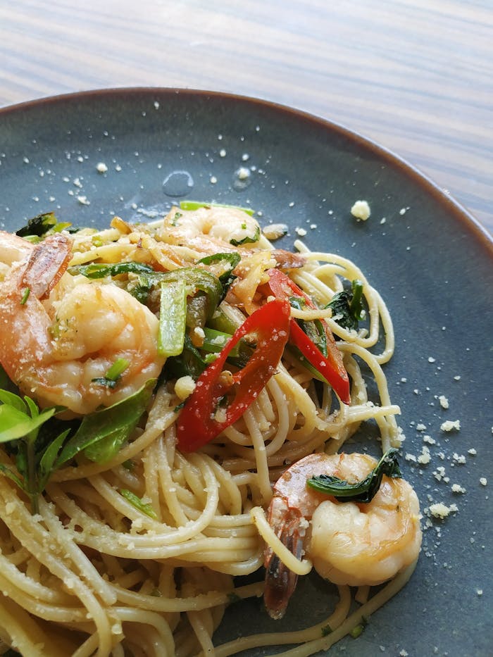 Appetizing shrimp pasta garnished with fresh chili and herbs in a close-up view.